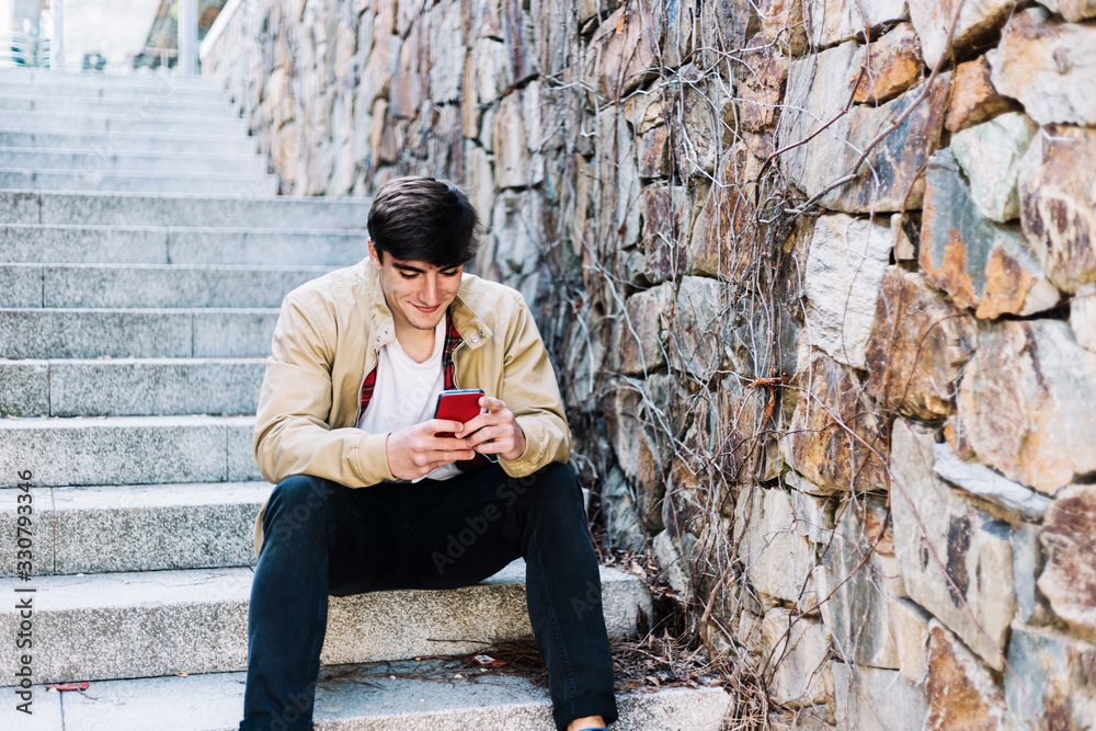 Young hispanic man using mobile phone while sitting outdoors