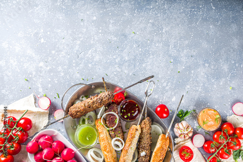 Summer bbq party. Shish kebab on a stick, from ground beef and chicken meat. Lula kebab, traditional Caucasian asian dish. With various sauces, spices and tomatoes, grey stone background, copy space a