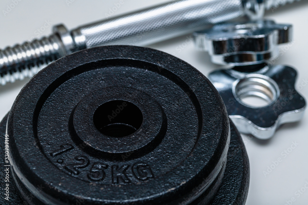 Close-up of four black weight training weights in focus stacked upon each other with handle and locks out of focus on a white background. Concept of training, fittness and excercise for healthy living Close-up of four black weight training weights in focus stacked upon each other with handle and locks out of focus on a white background. Concept of training, fittness and excercise for healthy living