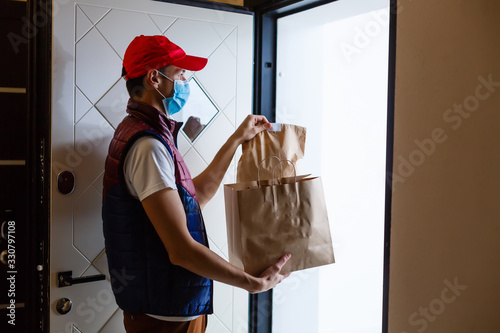 Delivery man holding paper bag with food on white background, food delivery man in protective mask