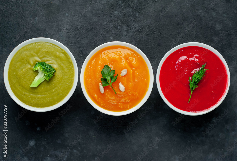 Set of vegetable soups. Broccoli, spinach, green peas soup. Pumpkin and carrot soup. Beetroot and carrot soup on a stone background with copy space for your text Set of vegetable soups. Broccoli, spinach, green peas soup. Pumpkin and carrot soup. Beetroot and carrot soup on a stone background with copy space for your text