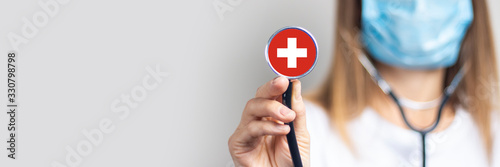 female doctor in a medical mask holds a stethoscope on a light background. Added flag of Switzerland. Concept medicine, level of medicine, virus, epidemic. Baner photo