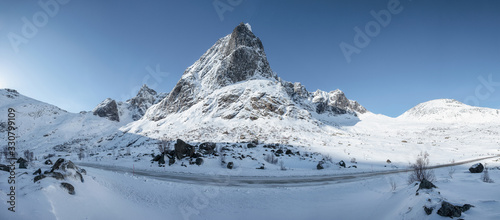 Panorama of snowy mountain range with blue sky and highway in Nordland