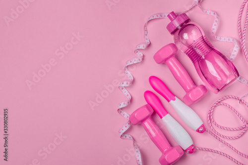 Dumbbells, bottle of water, jump rope and measuring tape on pink background