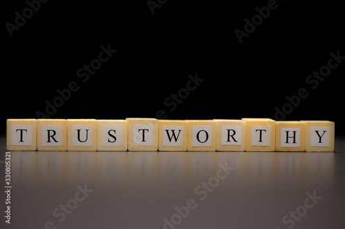 The word TRUSTWORTHY written on wooden cubes, isolated on a black background... photo