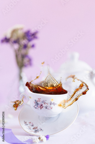 Flying black tea and levitating white cup on the purple background