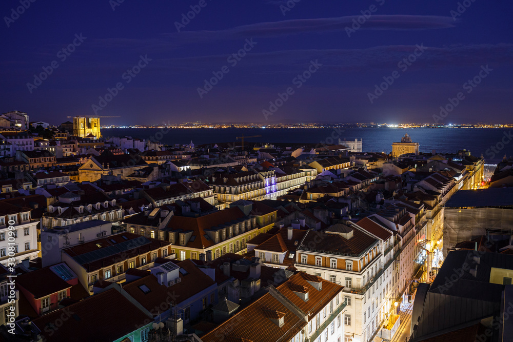 View of the lit Se Cathedral and Arco da Rua Augusta, buildings at the Baixa district and Tagus River in Lisbon, Portugal, from above at dusk.