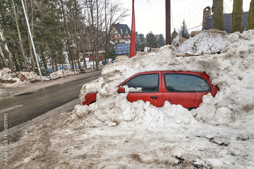 Red passenger car burried under the snow after heavy snowfall