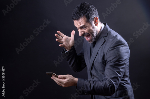 Uomo in abito discute animatamente al telefono, Isolato su sfondo nero