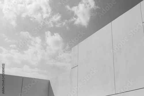 Modern architecture. Big white walls of the building against the blue sky and white clouds. Minimalistic design. Black and white photo