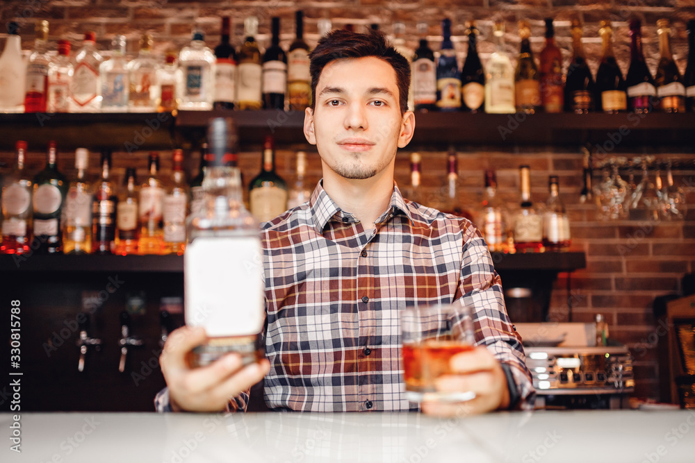 Barman holds out glass of whiskey with ice to male visitor. Concept rest in bar