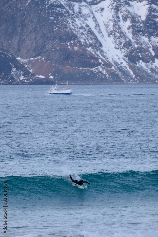 Obraz premium Surfing in cold ocean in Lofoten islands. Famous destination for surfers all around the world. Surfing between snowy mountains and arctic beaches. Surfers riding the waves in Norway. 