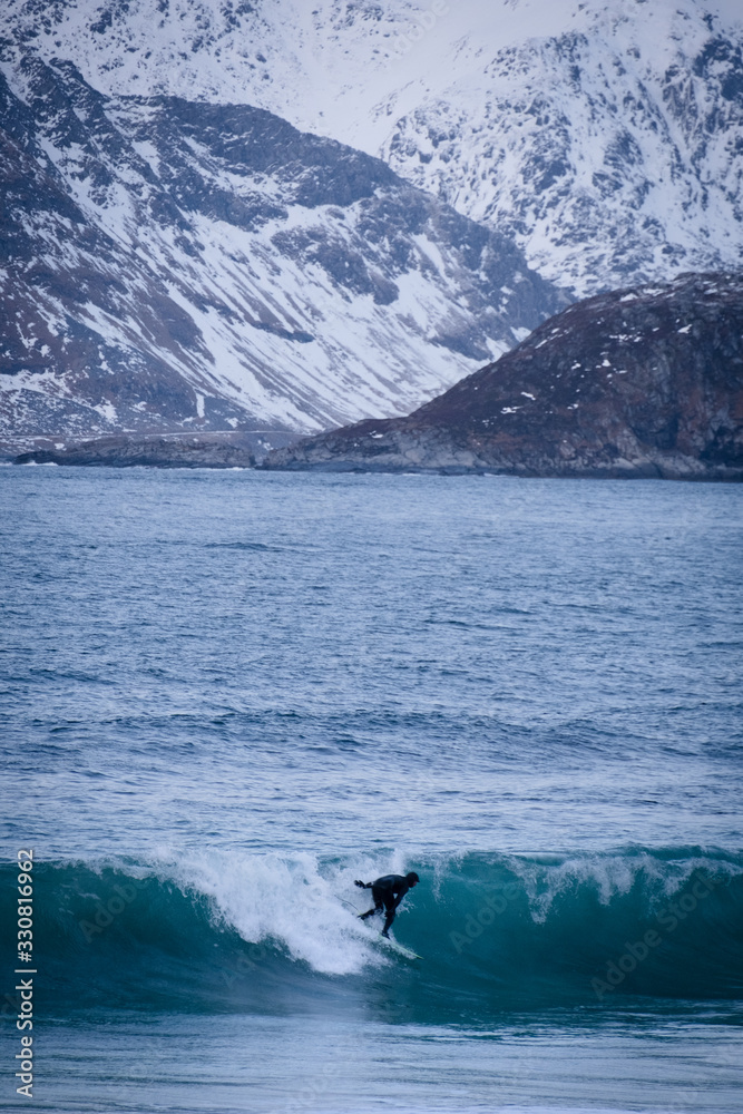 Surfing in cold ocean in Lofoten islands. Famous destination for surfers all around the world. Surfing between snowy mountains and arctic beaches. Surfers riding the waves in Norway. Surfing in cold ocean in Lofoten islands. Famous destination for surfers all around the world. Surfing between snowy mountains and arctic beaches. Surfers riding the waves in Norway.