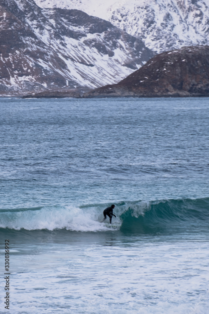 Obraz premium Surfing in cold ocean in Lofoten islands. Famous destination for surfers all around the world. Surfing between snowy mountains and arctic beaches. Surfers riding the waves in Norway. 