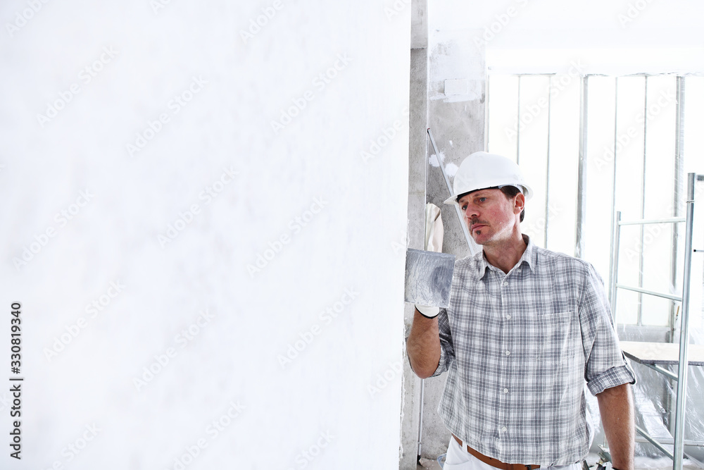 plasterer man at work with trowel plastering the wall of interior construction site wear helmet and protective gloves, scaffolding on background and copy space on white wall plasterer man at work with trowel plastering the wall of interior construction site wear helmet and protective gloves, scaffolding on background and copy space on white wall