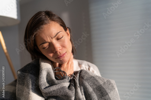 Coronavirus disease (COVID-19) symptoms are a runny nose, sore throat, cough, and fever. Corona virus illness can be more severe for some people. Asian woman with throat pain at home.