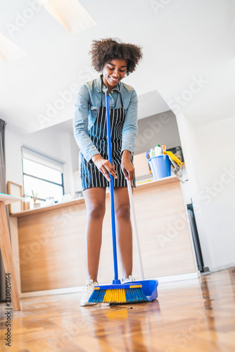 Afro woman sweeping floor with broom at home.