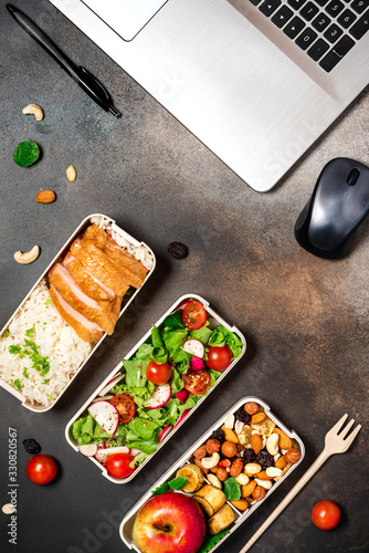 Lunch at the office or workplace. Lunch boxes with chicken, rice, salad, fruits and nuts on a dark desktop, top view. Healthy balanced office food in lunchboxes, flat lay