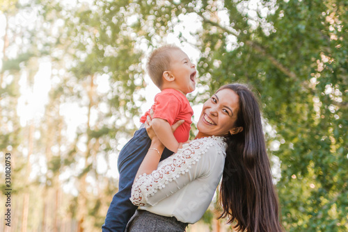  A happy young mother plays and has fun with her little son in the sun on a warm spring or summer day. The concept of a happy family, motherhood. Mother and child walk