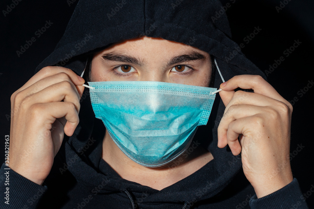 teenager in a hood puts on a disposable mask in the dark. Coronavirus,MERS-CoV,air contamination,Wuhan coronavirus 2019-nCoV,concept of Corona virus quarantine,Covid-19 teenager in a hood puts on a disposable mask in the dark. Coronavirus,MERS-CoV,air contamination,Wuhan coronavirus 2019-nCoV,concept of Corona virus quarantine,Covid-19