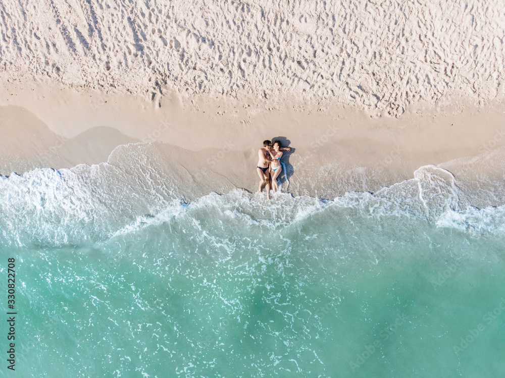 A couple in a swimsuit is lying on the shore of the azure sea in the sand shot from a quadrocopter