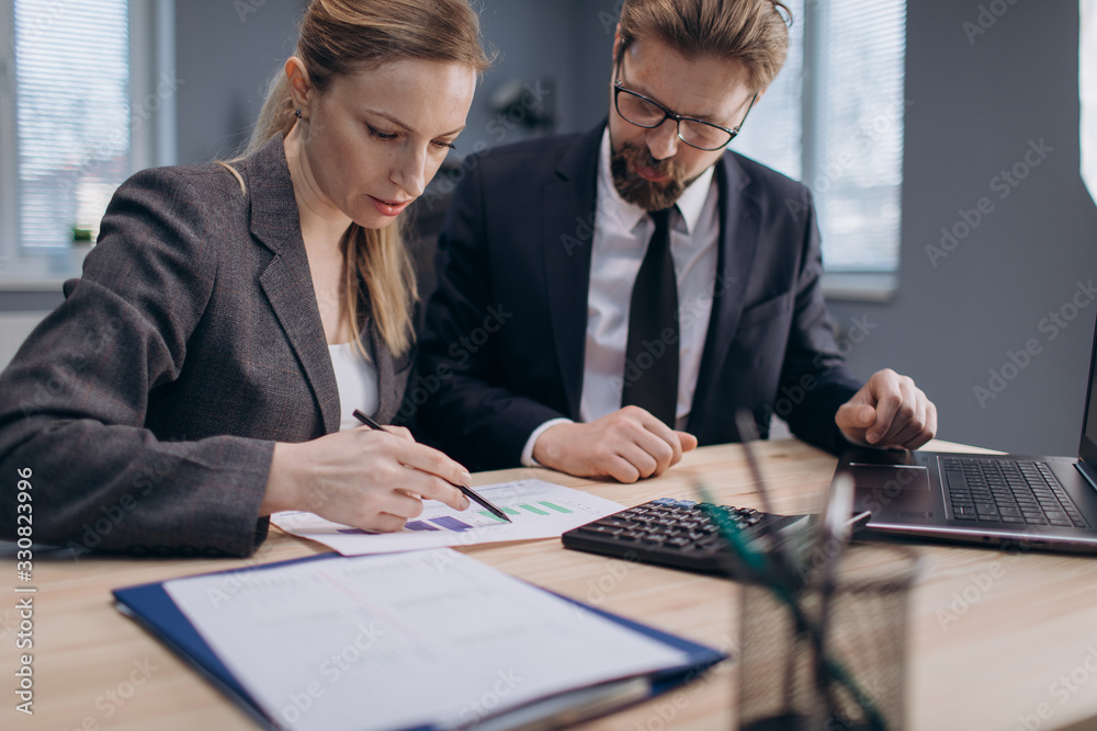 Professional company workers in business suits sitting at modern office and preparing financial report.Two mature partners working together on common project. Professional company workers in business suits sitting at modern office and preparing financial report.Two mature partners working together on common project.