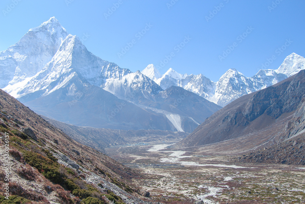 White snowy Ama Dablam mountain peak rises above mountain valley in Himalayas in the morning on the way to Everest base camp in Nepal. Clear blue sky. Theme of beautiful mountain landscapes.
