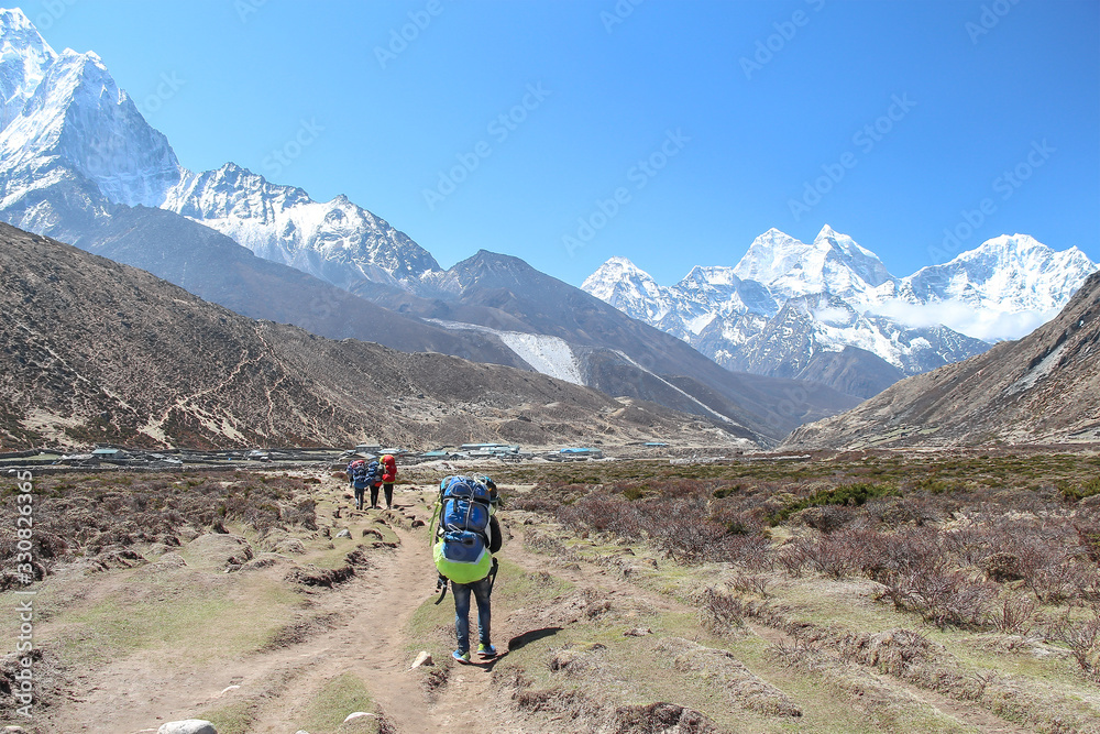 Back view. Nepalese sherpa porter walks carrying heavy bags towards Pheriche village in Himalayas on the way to Everest base camp. Ama Dablam mountain is visible in the background. Hiking theme.