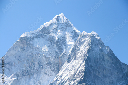 View of white snowy Ama Dablam mountain peak in Himalayas in the morning on the way to Everest base camp in Nepal. Clear blue sky. Theme of beautiful mountain landscapes.