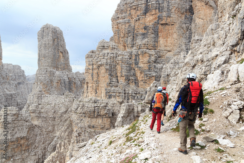 People hiking on via ferrata Sentiero delle Bocchette Centrale and mountain Campanile Basso in Brenta Dolomites, Italy