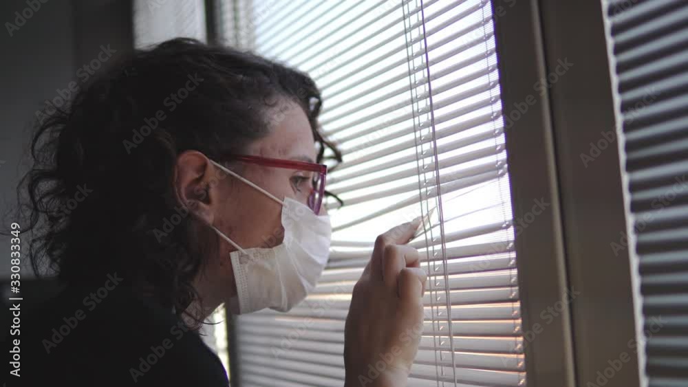 Infected corona virus covid-19 woman isolated in hospital room look over window blinds wearing protective mask Infected corona virus covid-19 woman isolated in hospital room look over window blinds wearing protective mask