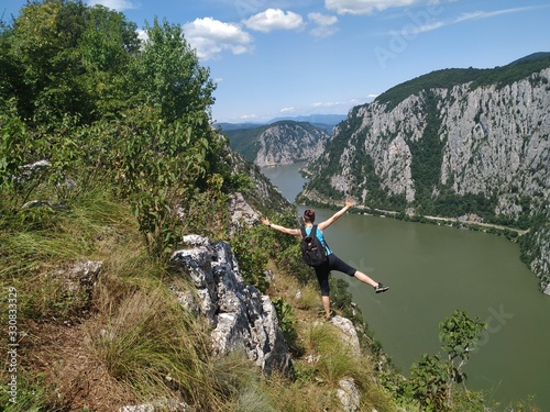 Girl standing on a rocky cliff hundred meters above the Danube Valley between Romania and Serbia, Yoga posing in the sun, meditating with arms wide open 