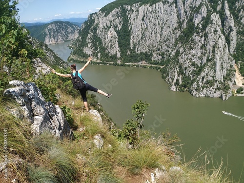 Girl standing on a rocky cliff hundred meters above the Danube Valley between Romania and Serbia, Yoga posing in the sun, meditating with arms wide open 