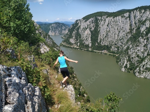 Girl standing on a rocky cliff hundred meters above the Danube Valley between Romania and Serbia, Yoga posing in the sun, meditating with arms wide open 