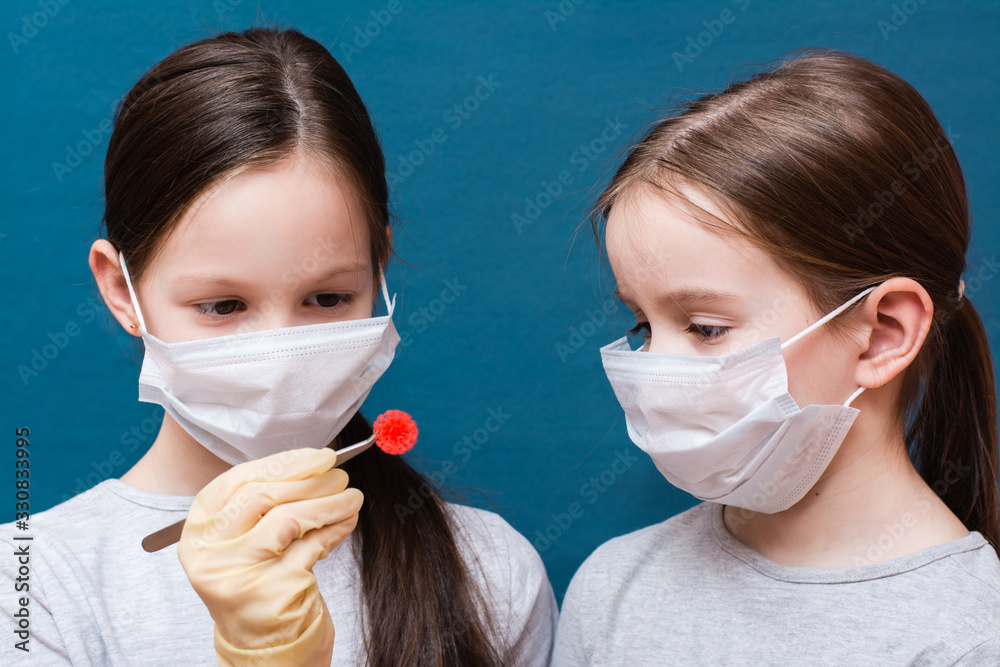 Two girls in medical masks are examining a coronavirus which one of them holds in tweezers. Hand in latex glove. Pneumonia pandemic