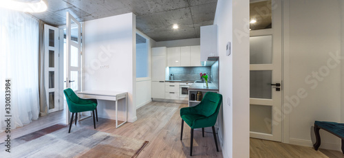 Modern interior of living room and kitchen in new studio apartment. Green chairs. White kitchen.