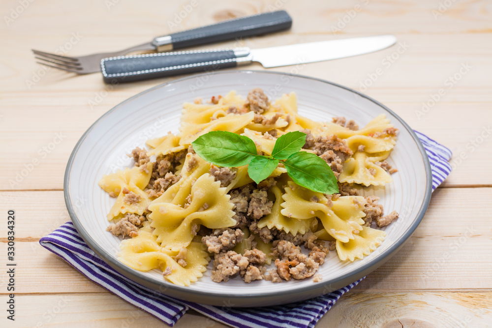 Ready-to-eat pasta navy with minced meat and basil leaves on a plate and cutlery on a wooden table. Russian cuisine