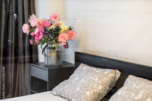 Modern interior of bedroom. Close-up of bouquet of flowers in the vase on the bedside. photo