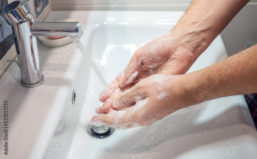 Washing hands with soap in sink to prevent corona virus, flu, hygiene to stop the spread of germs. Man's hand close up