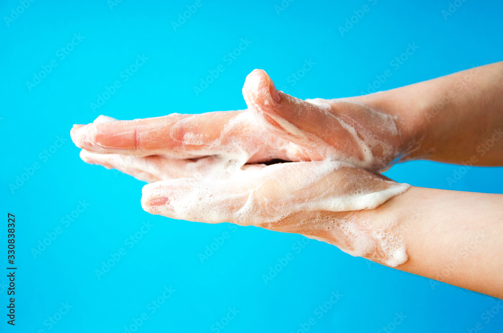 Women's hands are holding soap. Soap foam on the hands. Yellow soap in the hands. Woman washes soap with hands side view on a blue background. Virus protection.  COVID-19