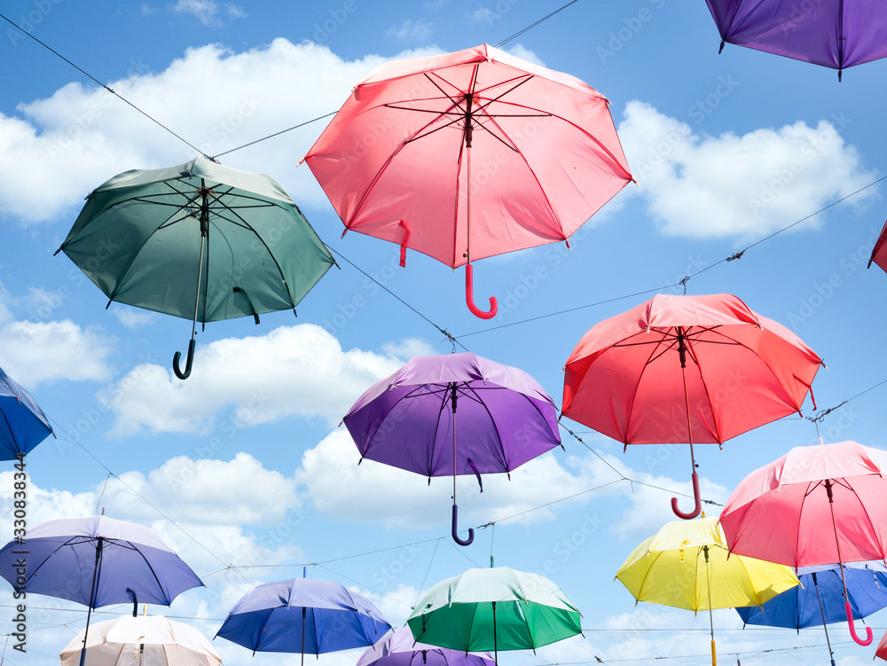 Multicolor parasol umbrella float in open air with sunny bright blue sky and white clouds ornament installation design for summer festival about happiness and freedom idea conceptual art