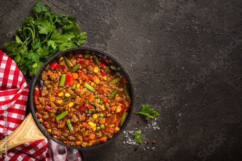 Chili con carne in skillet on dark stone table.