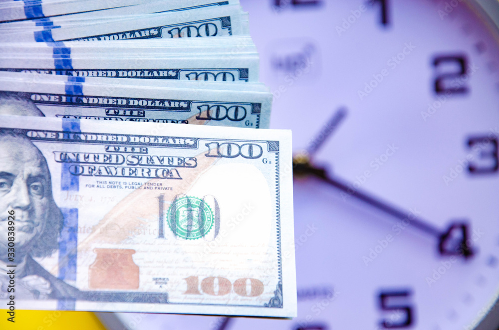 Fototapeta premium Analog white clock and dollars on a gray, yellow, blue background. Banknotes next to the clock, on top. Place for text. Business, are you ready? Copy Space
