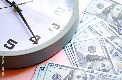 Analog white clock and dollars on a gray, yellow, blue background. Banknotes next to the clock, on top. Place for text.  Business, are you ready? Copy Space