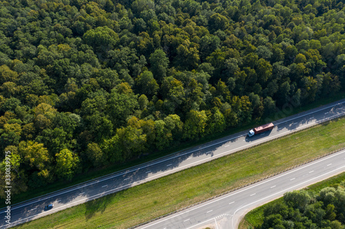 The truck is in a hurry to deliver the cargo, driving along a straight highway laid through the forest. Top view, shot on a drone.