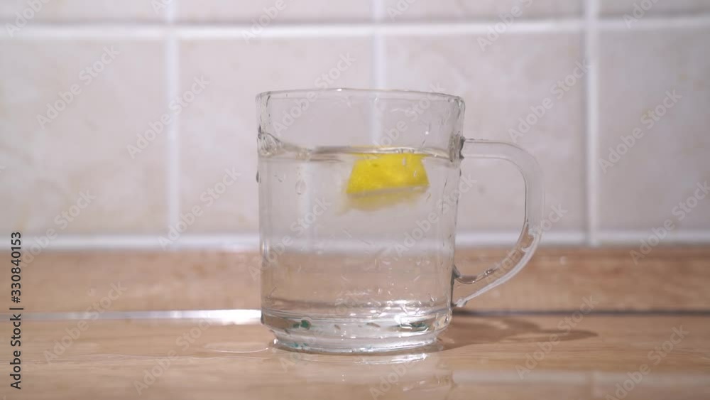On a wooden table is a clear glass of water, a woman 's hand throws diced lemons into the water.Slow motion On a wooden table is a clear glass of water, a woman 's hand throws diced lemons into the water.Slow motion