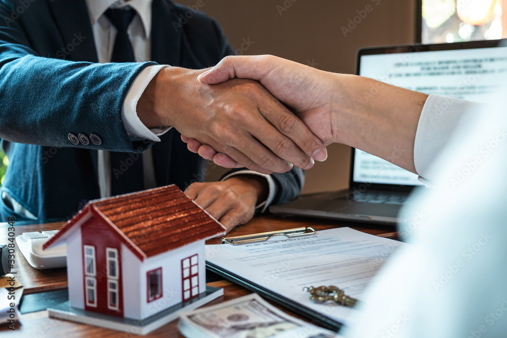 Real estate agent are shaking hands after good deal and giving house, keys to customer after signing contract to buy house with approved property application form