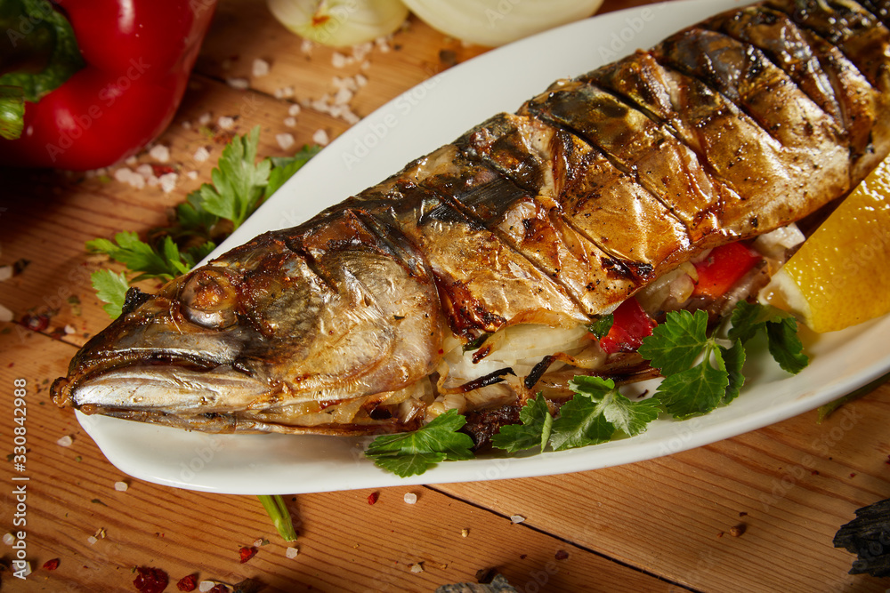 Appetizing grilled fish with vegetables on wooden background. Homemade smoked mackerel fish. Appetizing scomber prepared on tandoor (barbecue) on a brown rustic wooden table. Appetizing grilled fish with vegetables on wooden background. Homemade smoked mackerel fish. Appetizing scomber prepared on tandoor (barbecue) on a brown rustic wooden table.