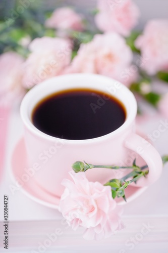 Pink cup of black coffee and pink carnation flowers on a light background