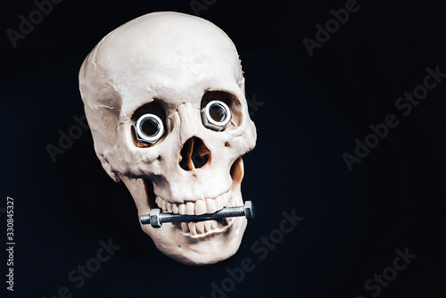 The human skull holds a steel bolt in its teeth , and instead of eyes it looks with large steel nuts